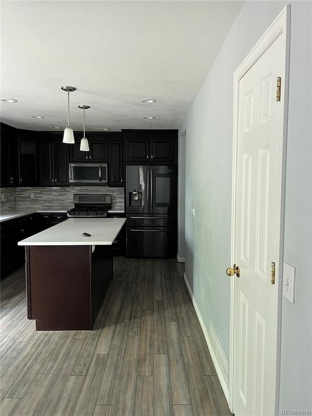 kitchen featuring stainless steel appliances, backsplash, a textured ceiling, hardwood / wood-style flooring, and hanging light fixtures