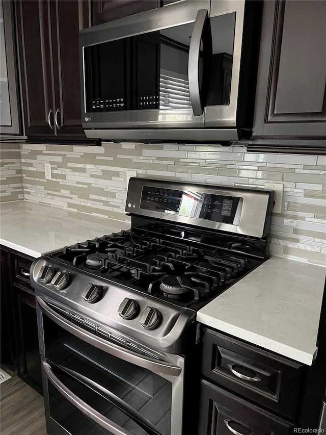 kitchen featuring dark brown cabinetry, tasteful backsplash, stainless steel appliances, and light stone countertops