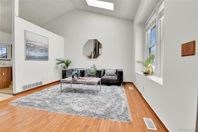 living room featuring visible vents, wood finished floors, and vaulted ceiling with skylight