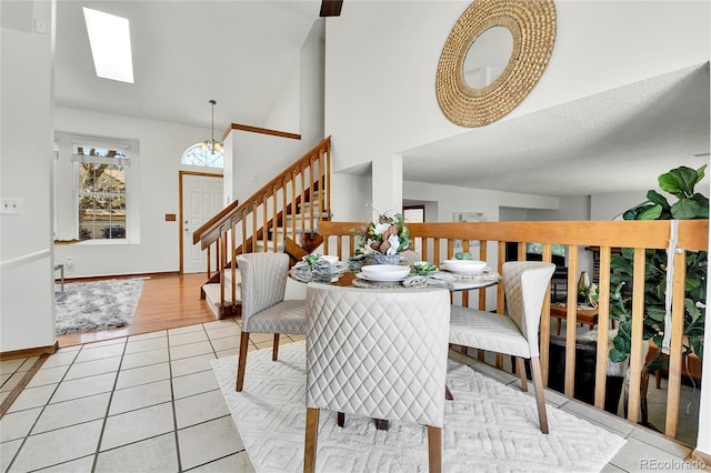 dining space with stairway, a skylight, light tile patterned flooring, and a towering ceiling
