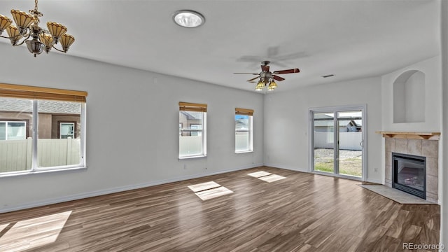 unfurnished living room with ceiling fan with notable chandelier, a fireplace, wood finished floors, visible vents, and baseboards