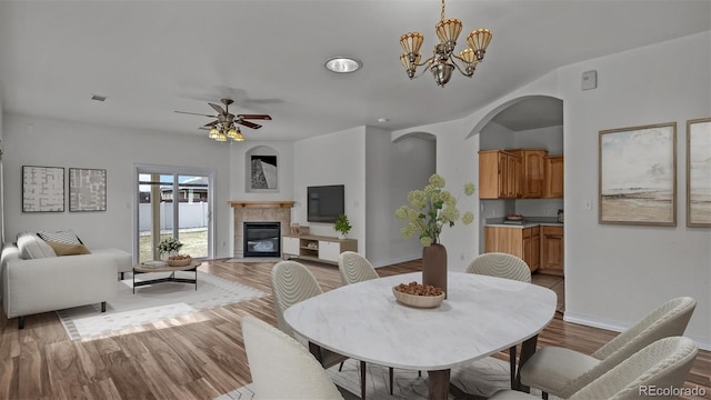 dining area featuring ceiling fan with notable chandelier, visible vents, baseboards, light wood-style floors, and a tiled fireplace