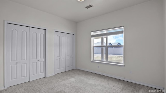 unfurnished bedroom with multiple closets, visible vents, carpet floors, and baseboards