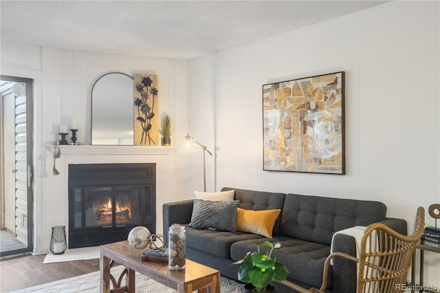 living room with a textured ceiling, a glass covered fireplace, and wood finished floors
