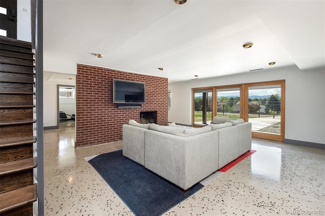 living room with stairs, a brick fireplace, baseboards, brick wall, and speckle patterned floor