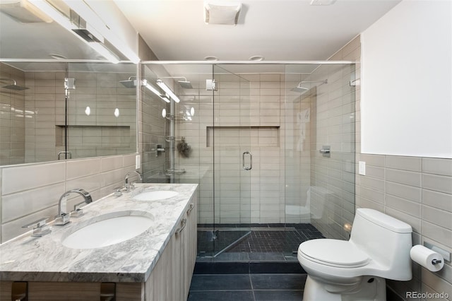 bathroom featuring tile patterned flooring, toilet, tile walls, a stall shower, and double vanity