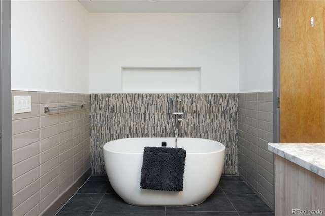 bathroom with tile walls, a freestanding bath, wainscoting, tile patterned flooring, and vanity