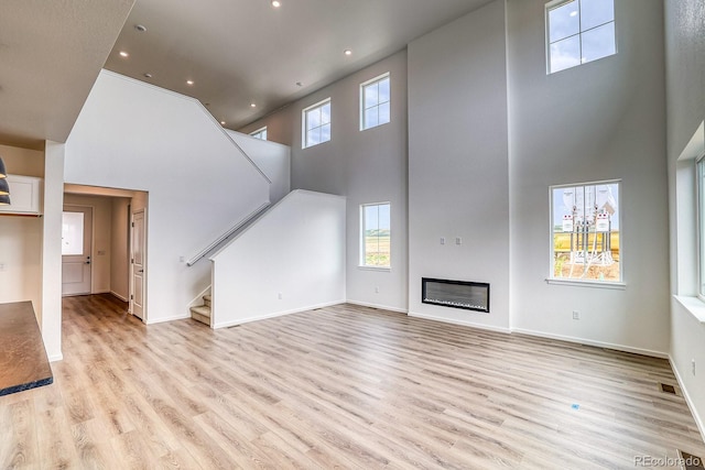 2197 S Jackson Gap St, Aurora, CO 80018 - unfurnished living room featuring a high ceiling, light wood finished floors, stairway, recessed lighting, and a glass covered fireplace