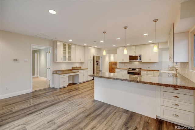 1275 Fairfax St, Denver, CO 80220 - kitchen featuring appliances with stainless steel finishes, light wood finished floors, dark stone counters, a peninsula, and glass insert cabinets