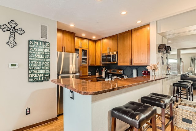 kitchen with tasteful backsplash, appliances with stainless steel finishes, a kitchen breakfast bar, and kitchen peninsula