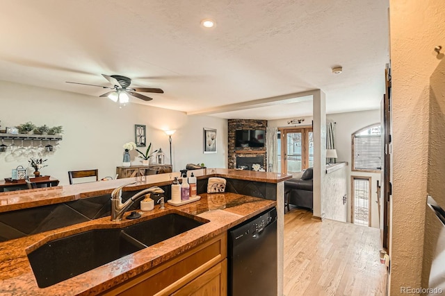 kitchen with a stone fireplace, stone countertops, black dishwasher, sink, and light hardwood / wood-style floors