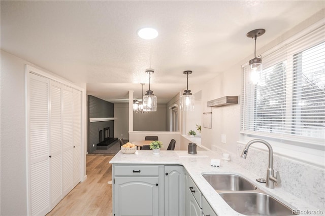 kitchen with light wood finished floors, a large fireplace, pendant lighting, a peninsula, and a sink