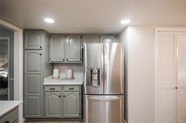 kitchen with a textured ceiling, gray cabinets, stainless steel refrigerator with ice dispenser, and light countertops