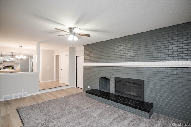 unfurnished living room featuring wood finished floors, visible vents, a fireplace, a textured ceiling, and ceiling fan with notable chandelier