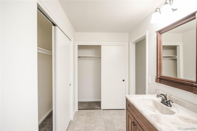 bathroom featuring baseboards, vanity, a spacious closet, and a textured ceiling