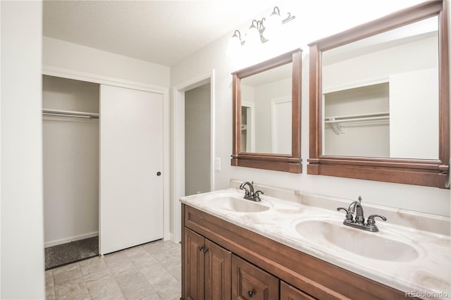 full bathroom featuring a walk in closet, double vanity, baseboards, and a sink