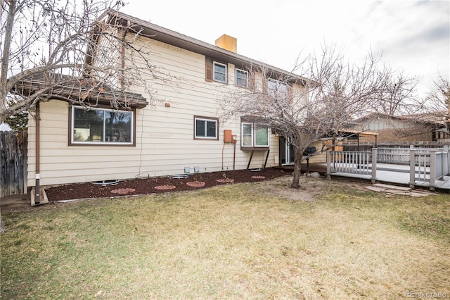 back of property featuring a yard, a wooden deck, a chimney, and fence