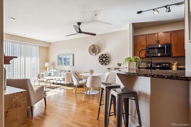 kitchen featuring ceiling fan, a kitchen breakfast bar, light hardwood / wood-style flooring, dark stone countertops, and appliances with stainless steel finishes