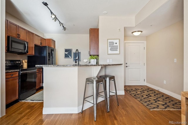 kitchen with kitchen peninsula, dark stone counters, wood-type flooring, a breakfast bar area, and black appliances