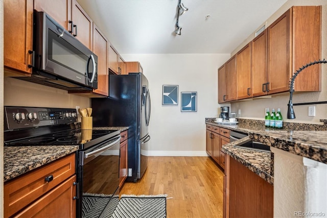 kitchen with track lighting, light hardwood / wood-style flooring, dark stone counters, and black electric range