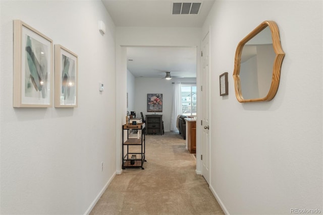 hall featuring baseboards, visible vents, and light colored carpet