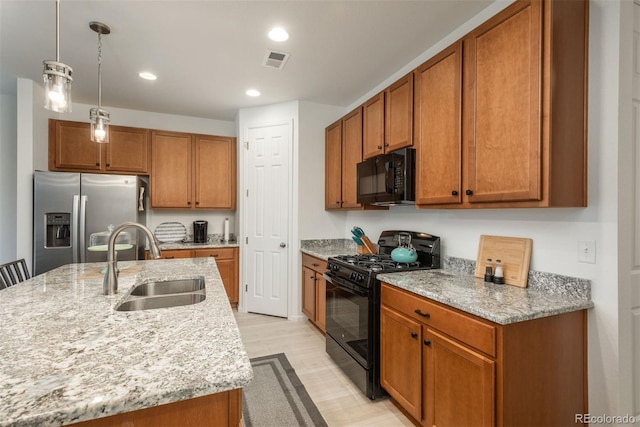 kitchen featuring a sink, visible vents, brown cabinets, black appliances, and an island with sink