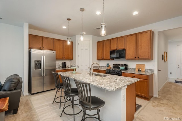 kitchen featuring a breakfast bar, a sink, light stone countertops, black appliances, and brown cabinetry