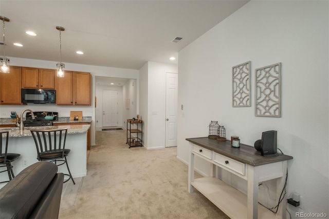 kitchen featuring black microwave, light colored carpet, stove, light stone countertops, and brown cabinetry