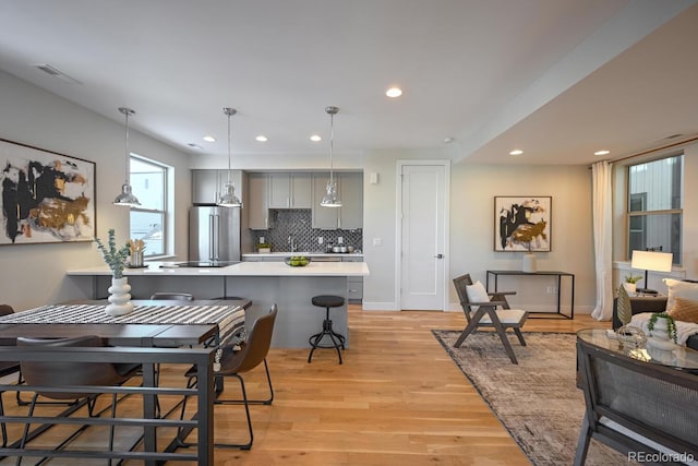 kitchen with pendant lighting, gray cabinetry, a kitchen bar, high end refrigerator, and light wood-type flooring