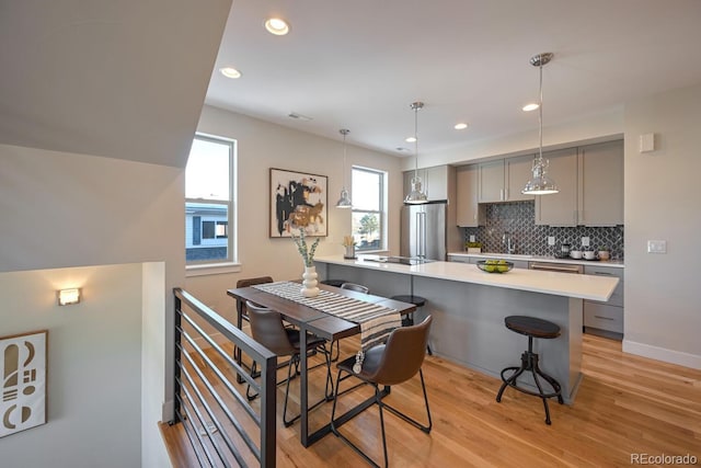 kitchen with a breakfast bar area, high end refrigerator, light wood-type flooring, gray cabinets, and backsplash