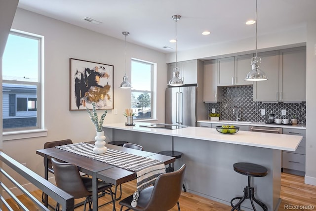 kitchen featuring a kitchen bar, gray cabinetry, high end refrigerator, light hardwood / wood-style flooring, and decorative backsplash