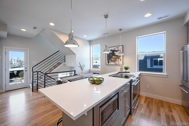 kitchen with hanging light fixtures, a center island, high end appliances, light hardwood / wood-style floors, and a kitchen bar