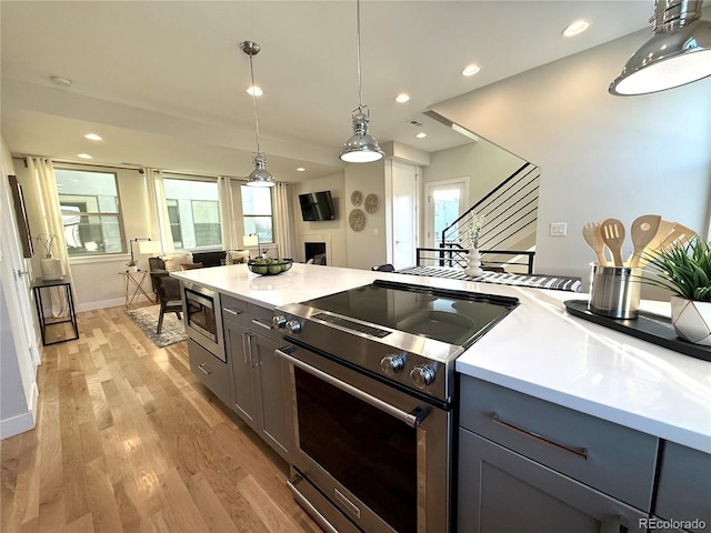 kitchen with stainless steel appliances, hanging light fixtures, plenty of natural light, and light hardwood / wood-style flooring