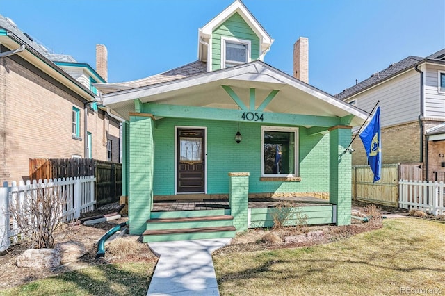 bungalow-style house with fence, covered porch, and brick siding