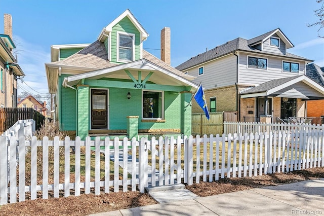 view of front of property featuring brick siding, a porch, a shingled roof, and a fenced front yard