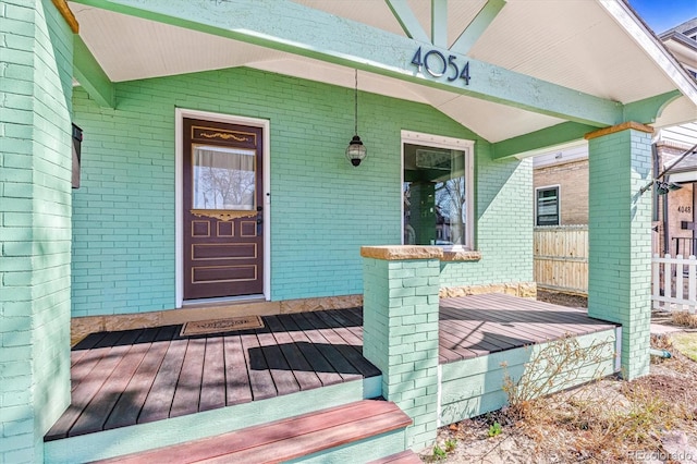 doorway to property featuring covered porch, fence, and brick siding