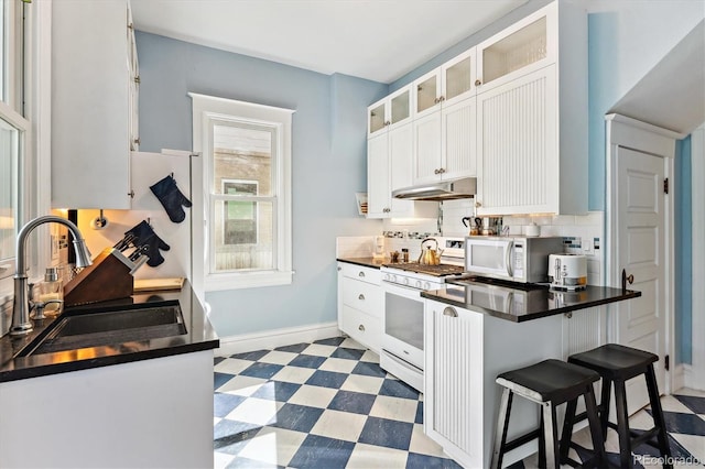 kitchen with tile patterned floors, a sink, under cabinet range hood, dark countertops, and white appliances