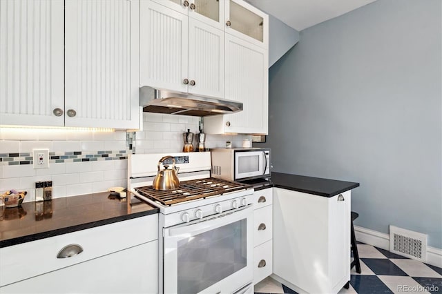 kitchen with tasteful backsplash, visible vents, dark countertops, under cabinet range hood, and white appliances