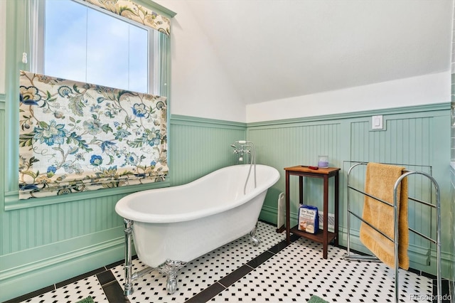 full bath with tile patterned flooring, wainscoting, a freestanding bath, and vaulted ceiling