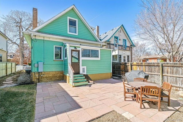 rear view of house with brick siding, entry steps, a chimney, a fenced backyard, and a patio area