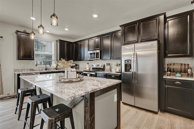 kitchen with pendant lighting, appliances with stainless steel finishes, light stone counters, light hardwood / wood-style floors, and a kitchen island