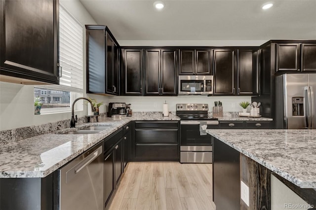 kitchen with sink, appliances with stainless steel finishes, light stone counters, dark brown cabinetry, and light hardwood / wood-style floors