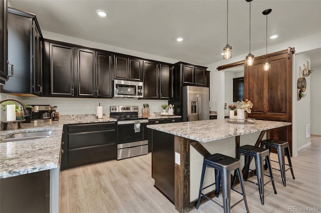 kitchen featuring sink, appliances with stainless steel finishes, a kitchen island, decorative light fixtures, and a barn door