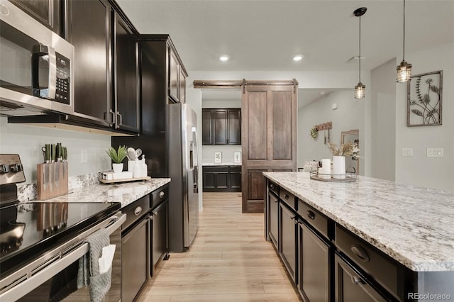 kitchen with decorative light fixtures, a barn door, light hardwood / wood-style floors, stainless steel appliances, and light stone countertops