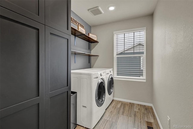 washroom featuring cabinets, washing machine and clothes dryer, and light hardwood / wood-style floors