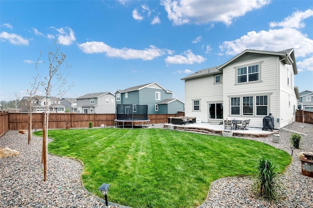 rear view of property featuring a trampoline, a yard, and a patio area