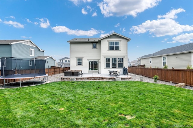 rear view of property featuring a trampoline, a yard, and a patio area