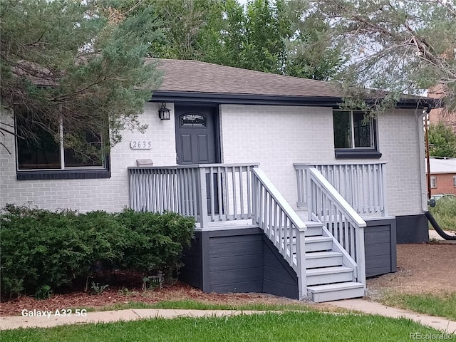 view of front of property featuring brick siding, stairway, and a shingled roof