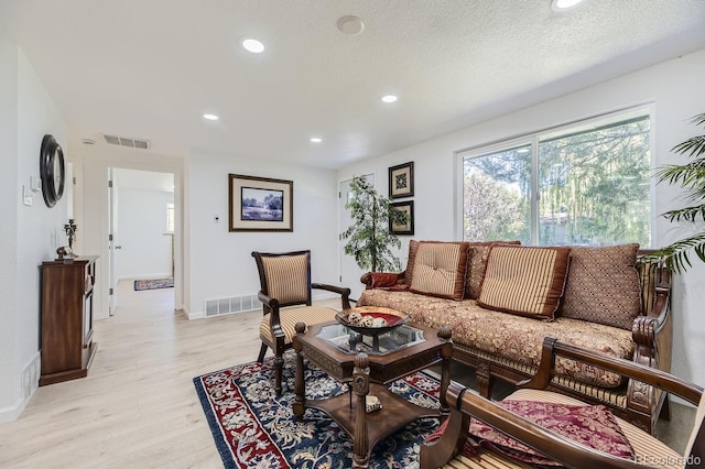 living area featuring light wood finished floors, visible vents, a textured ceiling, and recessed lighting