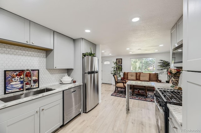 kitchen with gray cabinetry, decorative backsplash, appliances with stainless steel finishes, light wood-style floors, and a sink